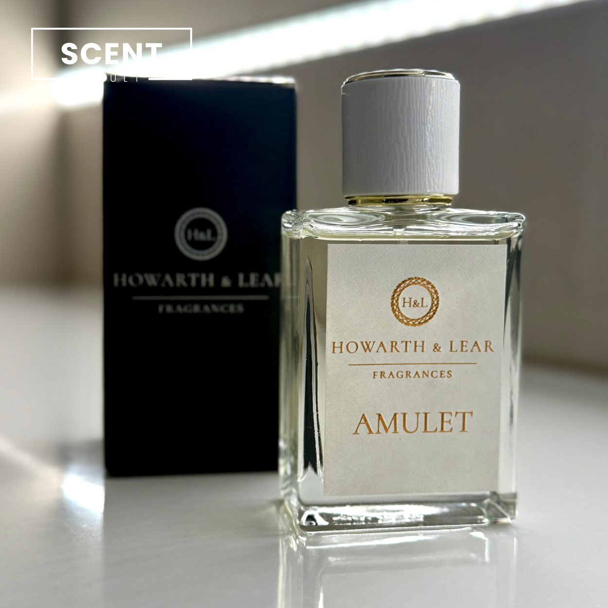 Howarth & Lear Fragrances Amulet perfume bottle on a reflective surface with packaging in the background.
