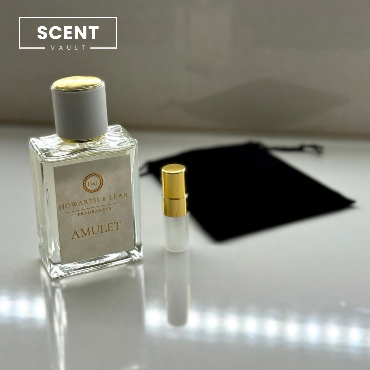 Perfume bottle labeled 'Amulet' by Howarth & Lear with a smaller bottle and black pouch on a reflective surface.