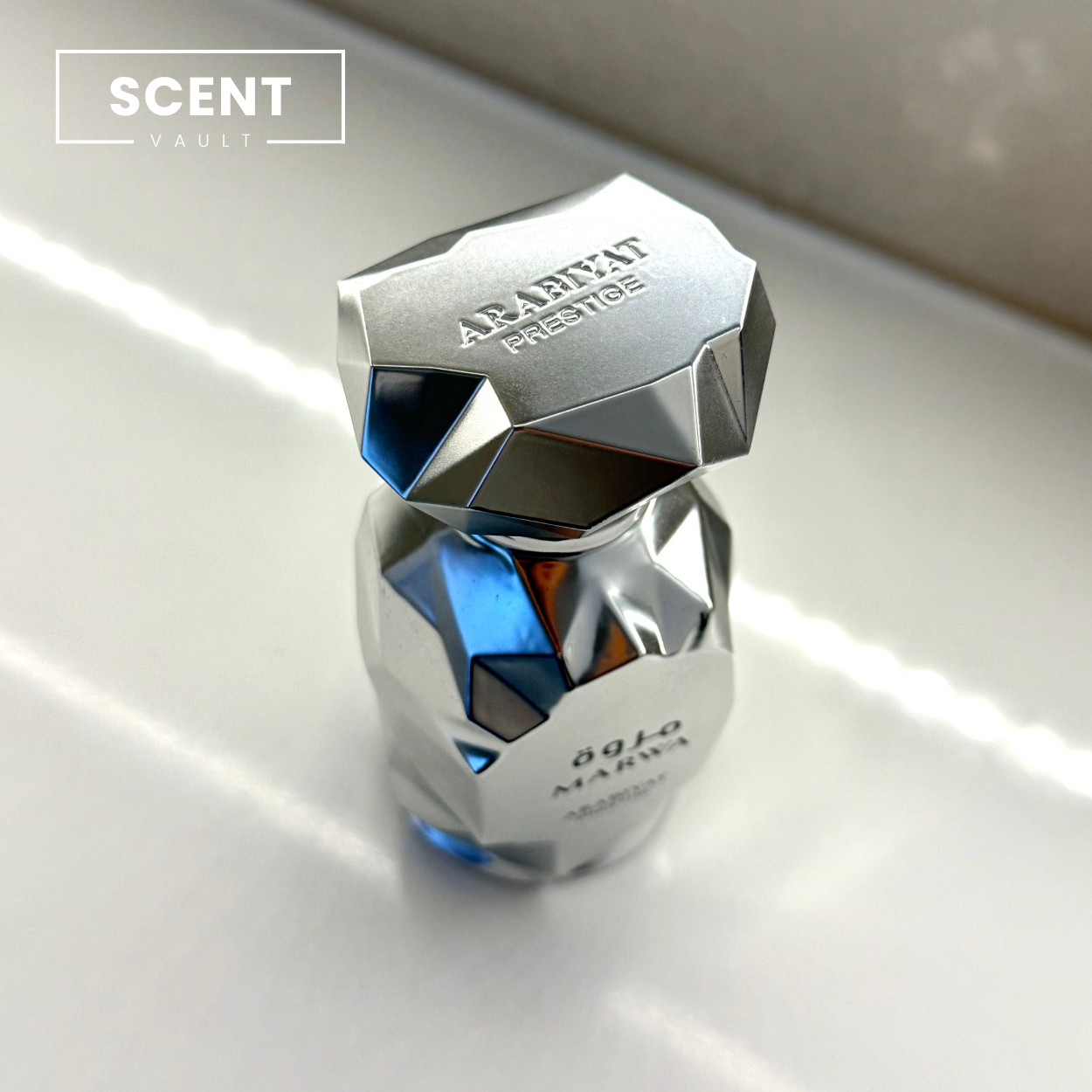 Silver and blue perfume bottle with 'SCENT VAULT' branding on a reflective surface.