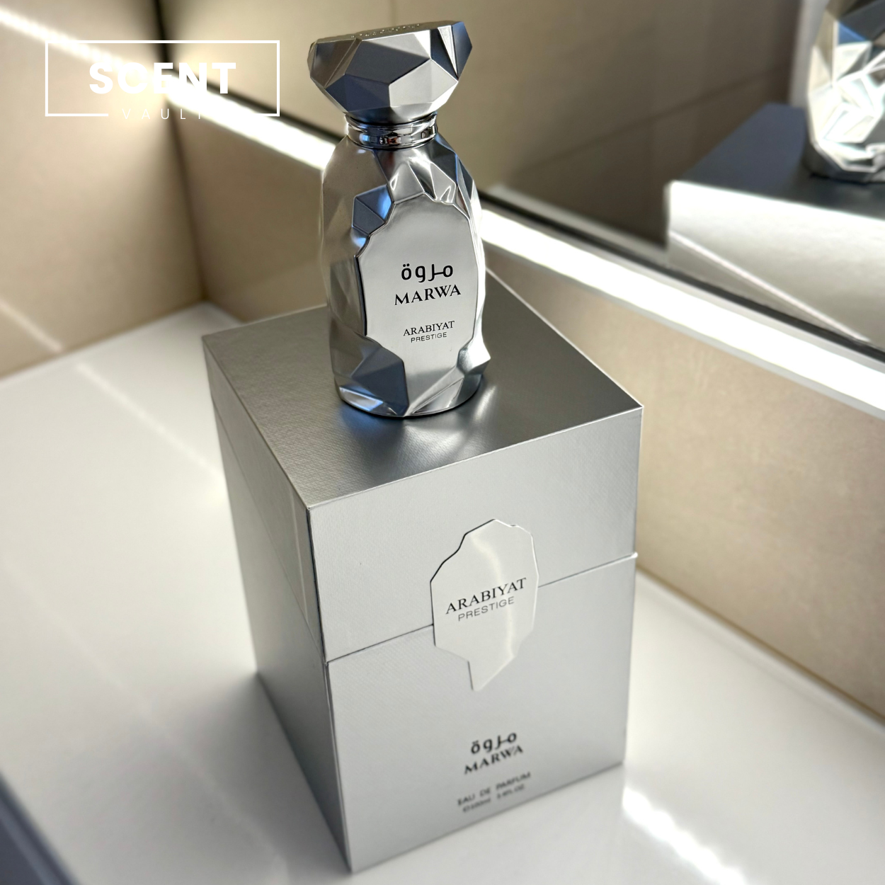 Silver perfume bottle and packaging on a reflective surface with 'Scent Vault' branding.