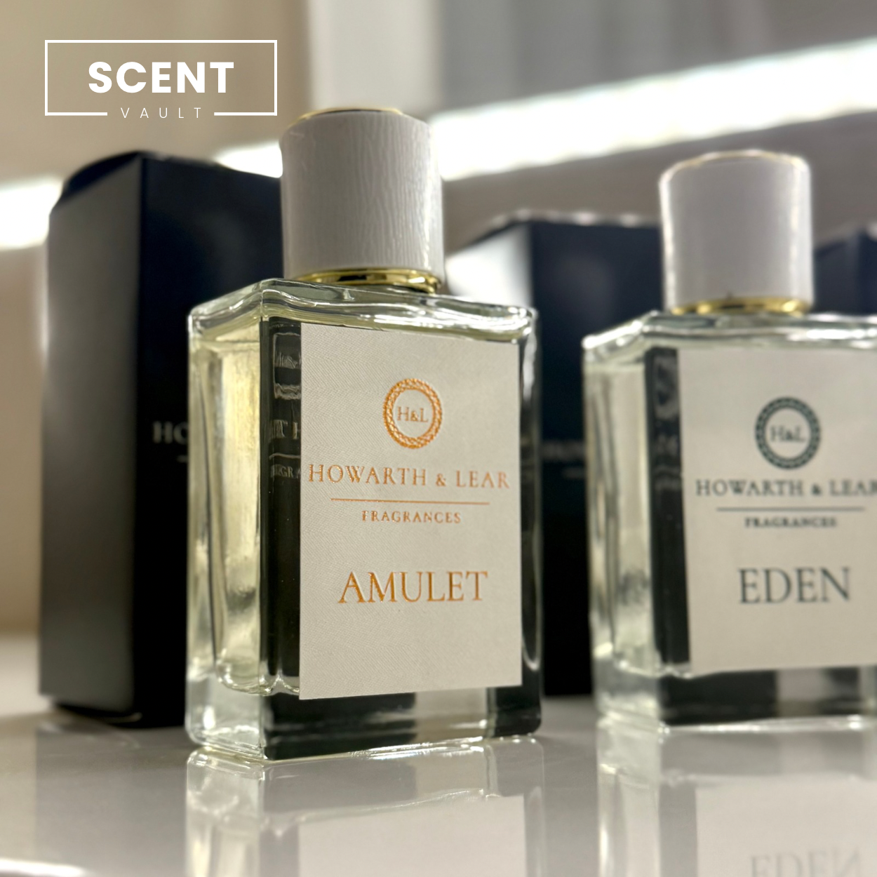 Two perfume bottles labeled 'Amulet' and 'Eden' by Howarth & Lea on a reflective surface.
