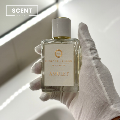 Hand holding a perfume bottle labeled 'Amulet' by Howard & Bear with 'Scent Vault' branding.
