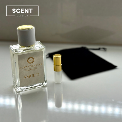 Perfume bottle labeled 'Amulet' by Howarth & Lear with a smaller bottle and black pouch on a reflective surface.