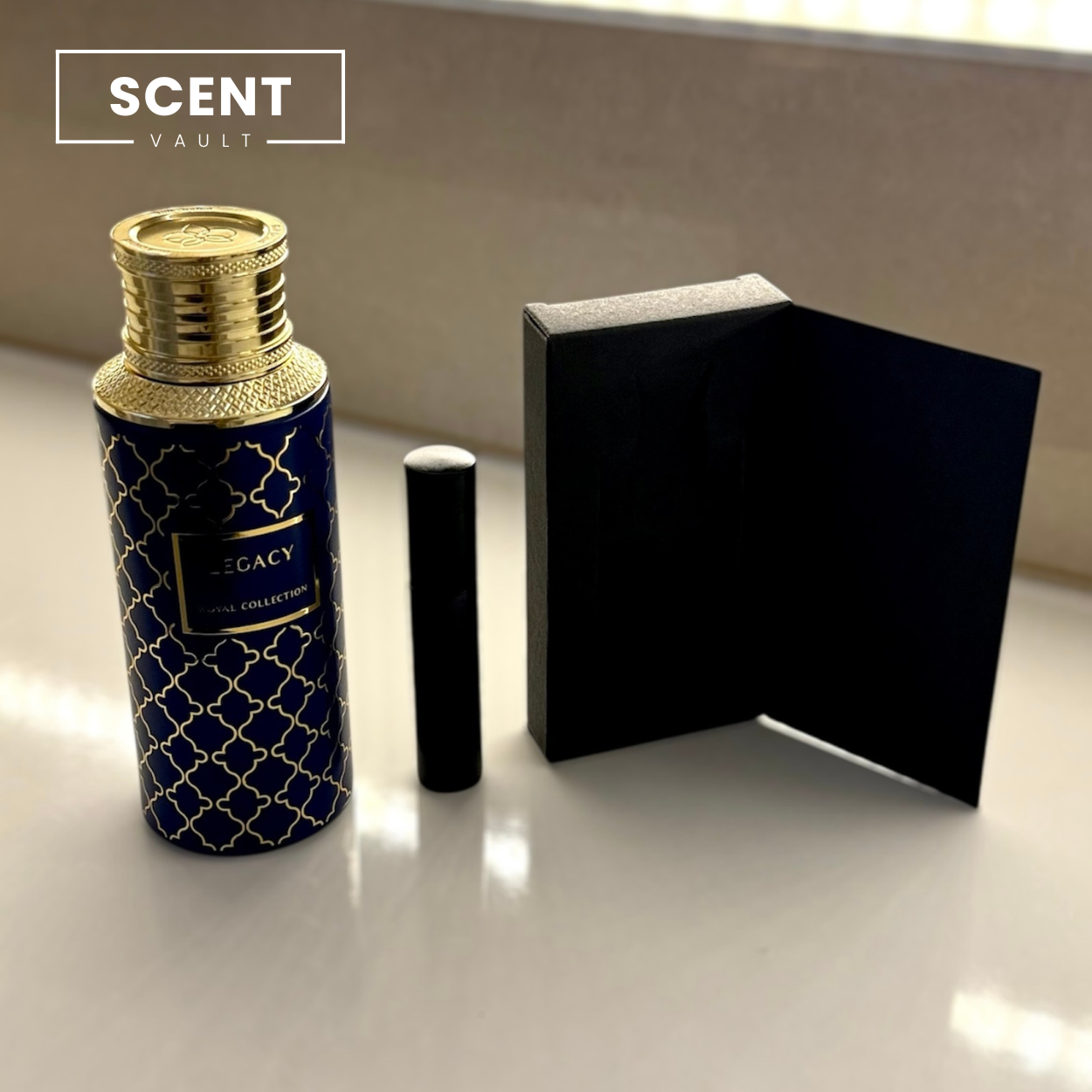 Perfume bottle with gold cap and blue design, next to a black box on a reflective surface.