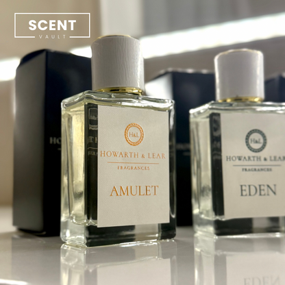 Two perfume bottles labeled 'Amulet' and 'Eden' by Howarth & Lea on a reflective surface.