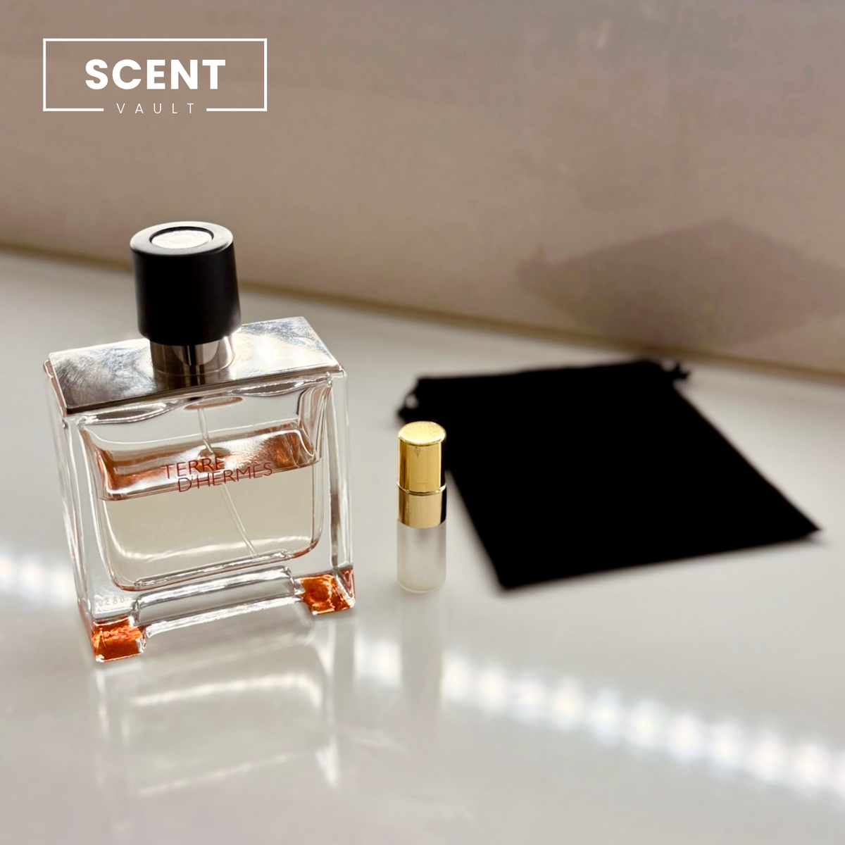 Hermès Terre d'Hermès Parfum bottle beside a decant spray vial and black velvet pouch - Scent Vault